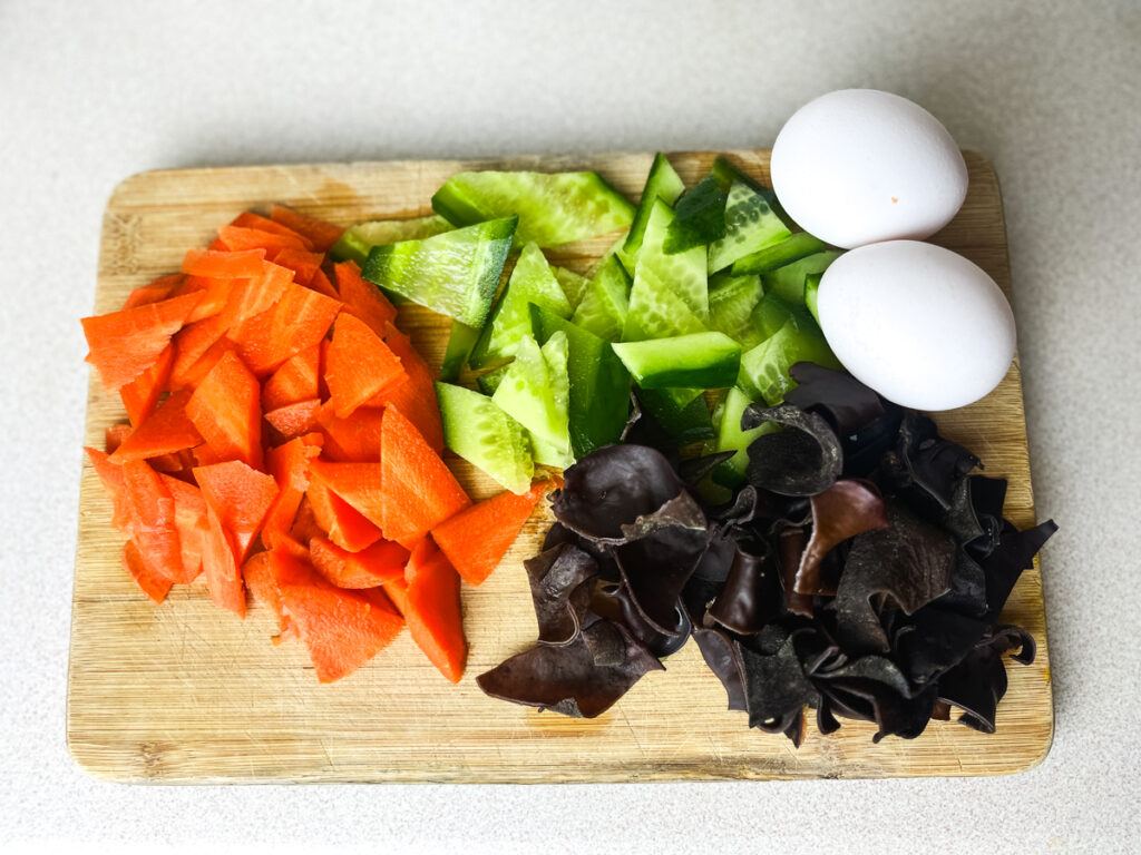 slices carrots cucumber and black fungus. Plus two eggs on a wooden chopping board