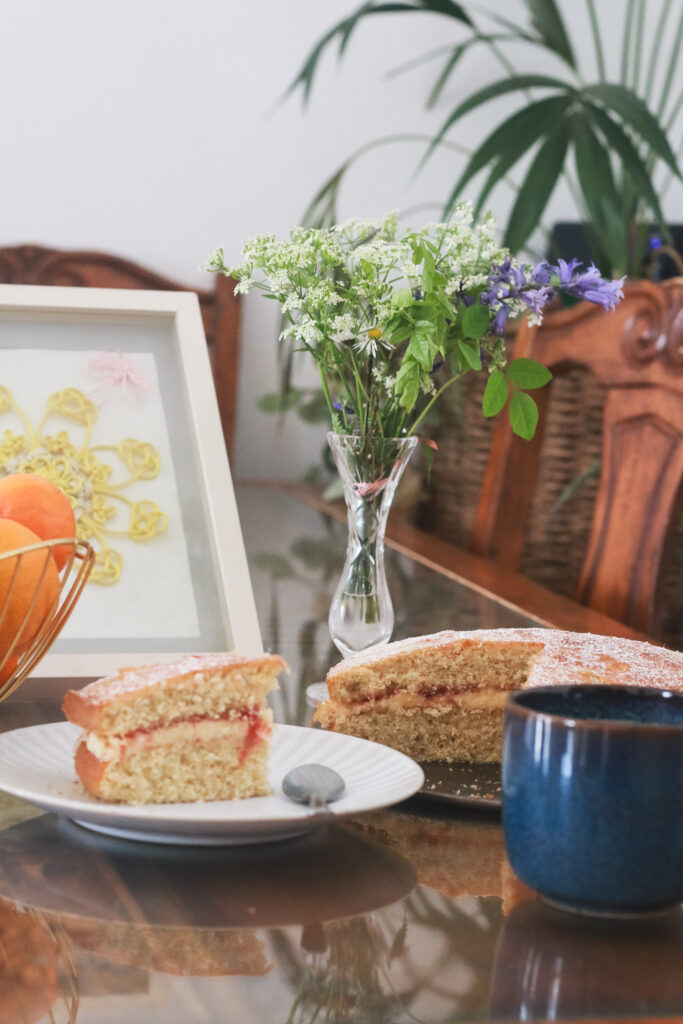 Victoria sponge cake made with coconut flour next to vase of flowers and cup of tea UK