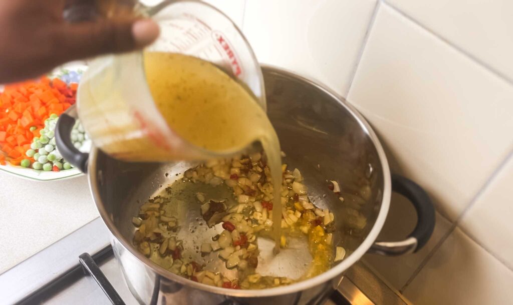 POURING chicken stock into a pot for nigerian coconut rice 