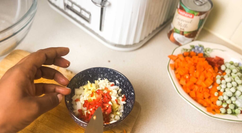 Cut vegetables for Nigerian Coconut Rice: carrots and peas plus bowl of chopped scotch bonnet, ginger and garlic